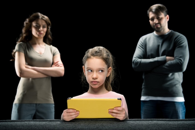 Fille à l'aide de tablette numérique tandis que les parents debout avec les bras croisés sur fond noir