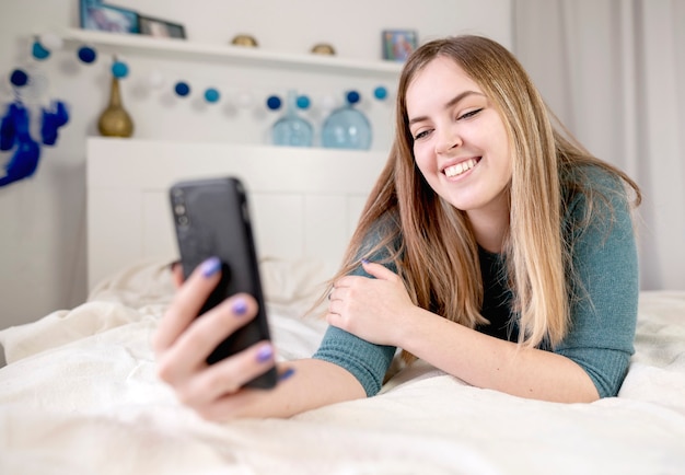 Fille à l'aide d'un téléphone portable sur le lit à la maison