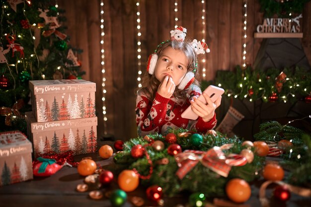 Fille à l'aide de téléphone près de l'arbre de Noël à l'intérieur décoratif.