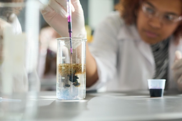 Fille ajoutant de l'encre violette dans du verre avec une substance chimique liquide transparente