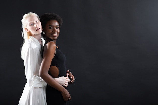 Fille albinos caucasienne et jeune femme afro-américaine étreignant sur le noir