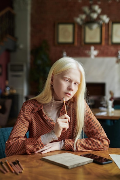 Fille albinos créative avec de longs cheveux blancs pensant à l'idée tout en esquissant