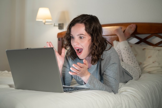Fille allongée sur le lit dans sa chambre à l'aide de l'ordinateur surpris Femme lors d'un appel vidéo dans un ordinateur portable