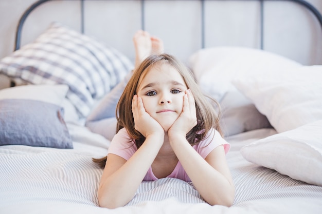 Fille allongée sur le lit, petite fille se reposant parmi les oreillers et les couvertures, rêves