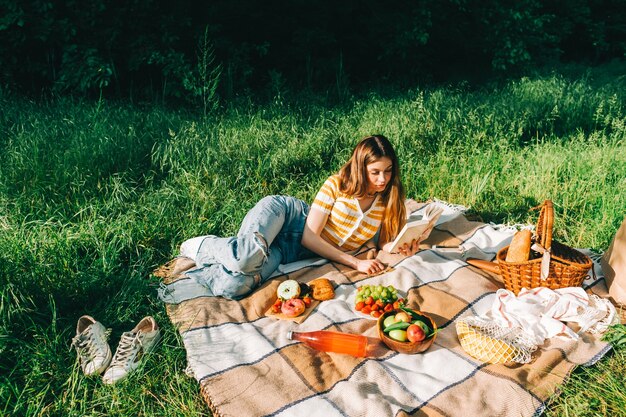 Fille allongée près des fruits frais, des baies, des boissons et de la boulangerie sur une couverture de pique-nique à l'extérieur