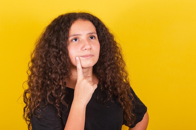 Fille d'Amérique latine brésilienne pour les cheveux afro fond jaune expression de doute pensant questionnant le doigt sur la joue