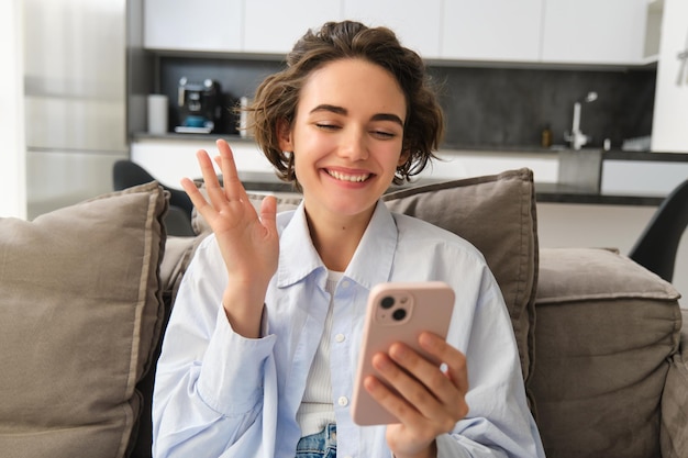 Une fille amicale parle sur des chats vidéo sur téléphone portable avec un ami agite la main à la caméra du smartphone se trouve sur