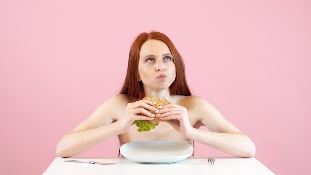 Une fille anorexique maigre mange avidement un hamburger. Troubles de l'alimentation. Anorexie