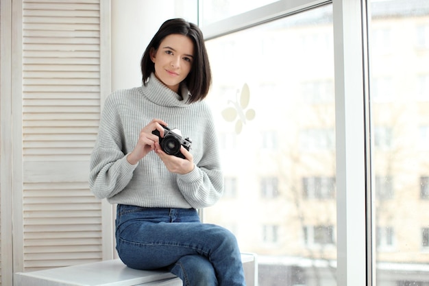 Fille avec un appareil photo assis près de la fenêtre