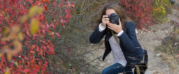 Une fille avec un appareil photo dans ses mains dans une pose amusante fait un cadre Paparazi avec un appareil photo dans ses mains sur une épidémie dans les montagnes