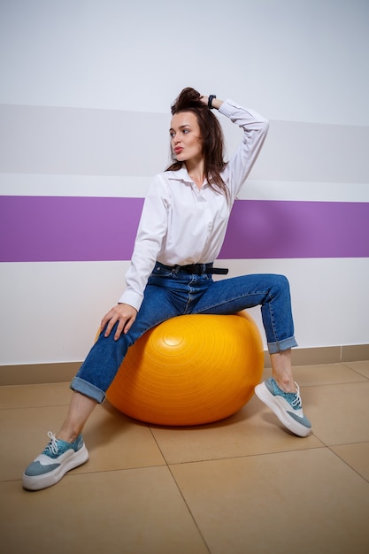 Une fille d'apparence européenne avec différentes émotions sur son visage est assise sur un ballon pour un gymnaste. Jolie jeune femme brune souriante et s'amuser