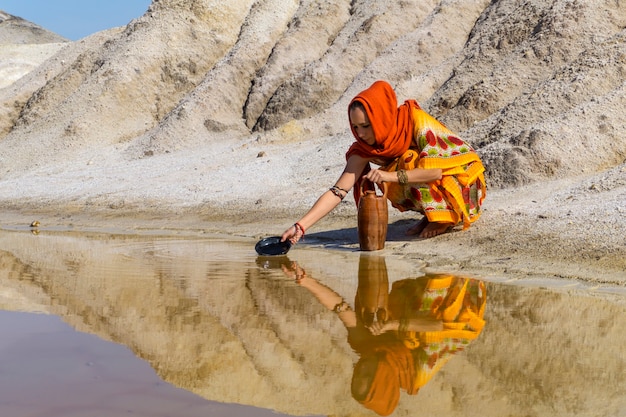 Fille d'apparence orientale remplit le pichet avec de l'eau d'une source dans la zone aride