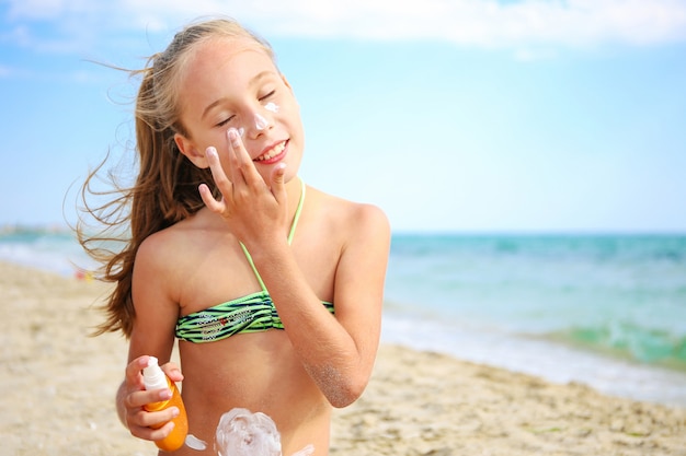 Fille appliquant un écran solaire protecteur sur le visage.