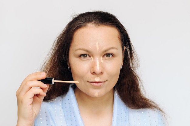 La fille applique un correcteur de lumière anti-cernes sur le visage dans les coins des yeux