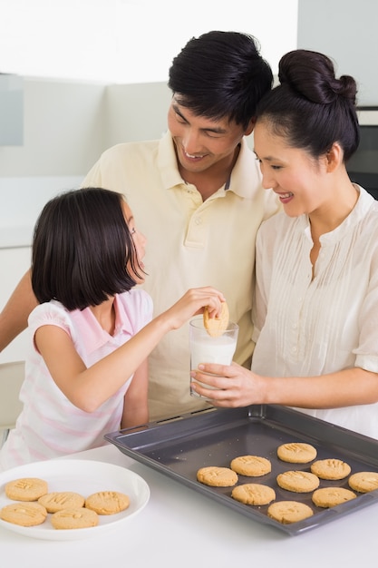 Fille en appréciant les cookies et le lait avec les parents dans la cuisine