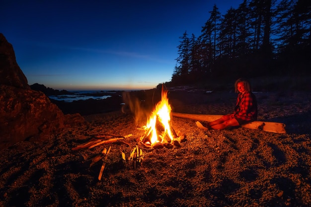 Fille appréciant un feu de camp sur la plage pendant un coucher du soleil vibrant d'été