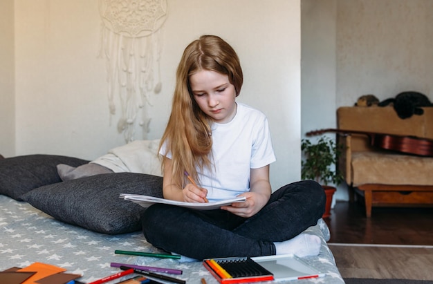 La fille après l'école joue à la maison dessine avec des crayons et des feutres