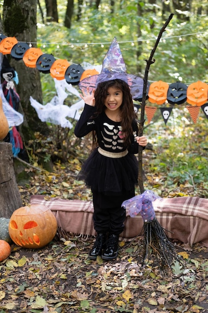 Fille arabe en costume d'halloween et chapeau de sorcière avec balai dans la décoration d'halloween en plein air
