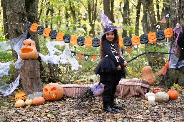 Fille arabe en costume d'halloween et chapeau de sorcière avec balai dans la décoration d'halloween en plein air