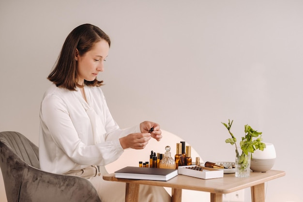 La fille aromathérapeute est assise dans son bureau et tient une bouteille d'huiles aromatiques il y a des huiles essentielles sur la table