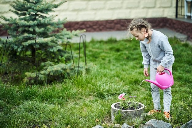 Fille arrosant un parterre de fleurs d'un arrosoir dans le jardin