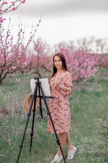 Fille artiste peint un verger de pêchers dans un printemps de verger de pêchers