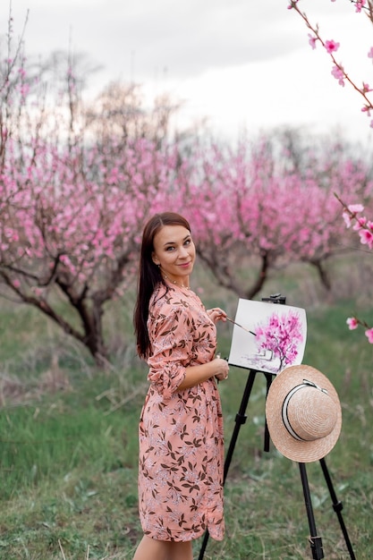 Fille artiste peint un verger de pêchers dans un printemps de verger de pêchers