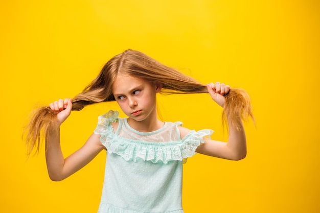 Fille artistique montre ses émotions l'enfant se tient sur un fond jaune dans un beau dr turquoise