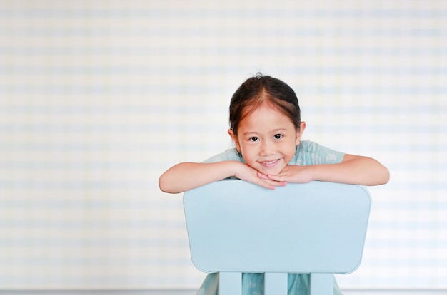 Fille asiatique d&#39;âge préscolaire heureux enfant asiatique dans une salle de jardin d&#39;enfants pose sur une chaise en plastique.