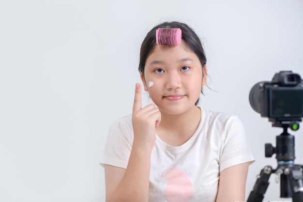 Fille asiatique appliquant le fond de teint sur la joue et enregistrant une vidéo sur un appareil photo moderne