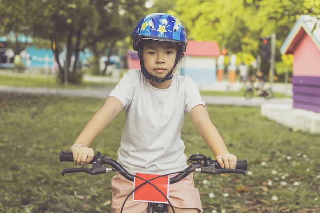 Fille asiatique apprend à faire du vélo dans le parc. Portrait d'un enfant mignon à vélo.