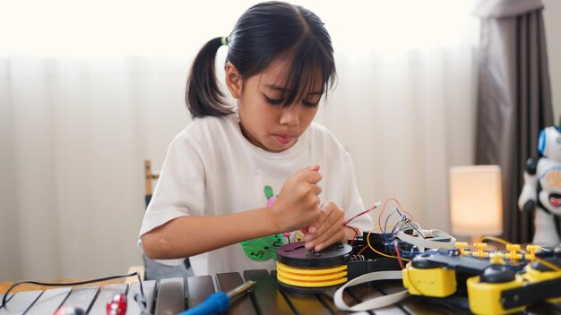 Fille asiatique assemblant des pièces de robots à la maison apprenant les STEM et l'électronique développant des compétences en ingénierie pensée logique et résolution de problèmes grâce à l'enseignement du codage manuel pour les enfants