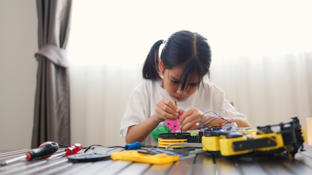 Fille asiatique assemblant des pièces de robots à la maison apprenant les STEM et l'électronique développant des compétences en ingénierie pensée logique et résolution de problèmes grâce à l'enseignement du codage manuel pour les enfants