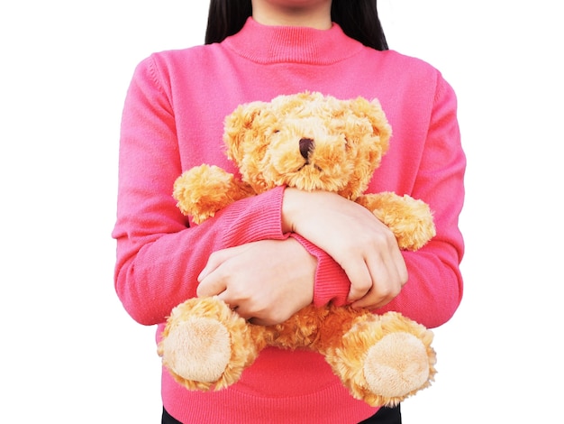 Fille asiatique aux cheveux longs portant une chemise rose et tenant un ours en peluche brun dans son bras, isolé sur fond blanc.