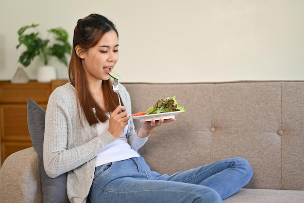 Fille asiatique en bonne santé mangeant sa salade saine tout en se relaxant dans son salon