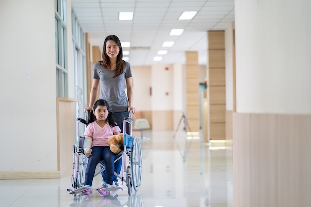 Fille asiatique avec un bras cassé portant un plâtre sur fauteuil roulant avec sa mère à l'hôpital