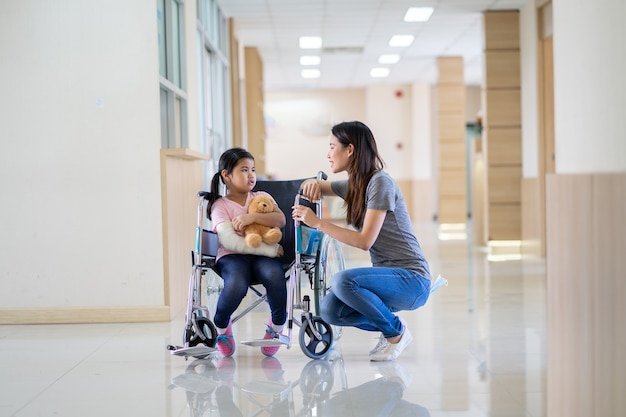 Fille asiatique avec un bras cassé portant un plâtre sur fauteuil roulant avec sa mère à l'hôpital