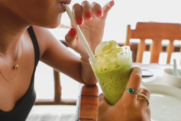 Fille asiatique buvant un régime de désintoxication sain et un smoothie au thé vert à la main avec de la crème blanche sur