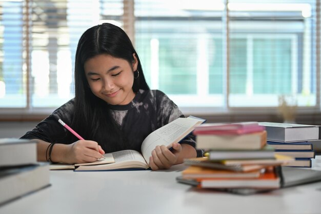 Fille asiatique concentrée écrivant sur un cahier et faisant ses devoirs dans le salon Concept d'éducation