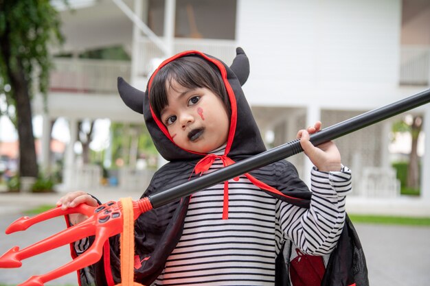 Fille asiatique d'enfant dans le costume de démon tenant le trident noir et rouge, concept heureux d'halloween