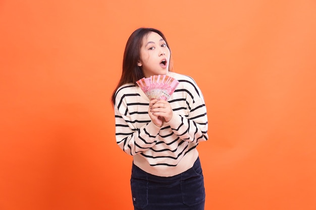 Photo une fille asiatique avec une expression choquée à la caméra se tient avec les deux mains tenant plusieurs roupies