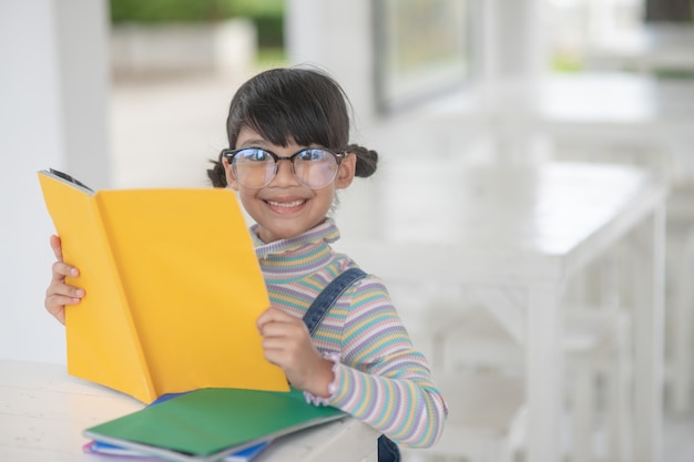 Fille asiatique heureuse lisant un livre sur la table