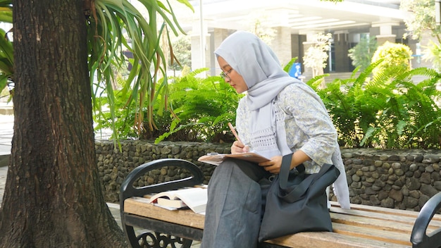 Une fille asiatique en hijab écrit des notes dans le jardin du campus