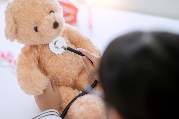 Fille asiatique jouant avec son ours en peluche patient dans un jeu de médecin à l'aide d'un stéthoscope Les enfants veulent être un médecin pédiatre