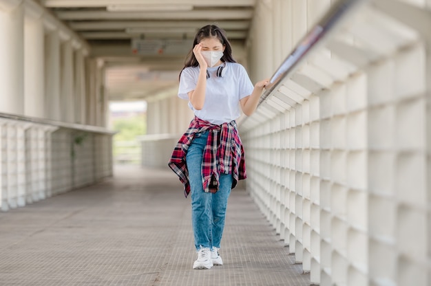 Une fille asiatique portant un masque marche sur un viaduc avec des maux de tête, un évanouissement soudain dû à des conditions débilitantes et de la fièvre due au coronavirus.