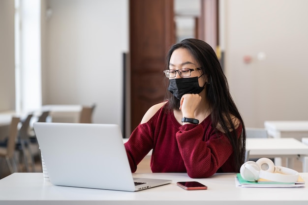 Une fille asiatique porte un masque médical en classe universitaire étudiant sur un ordinateur portable dans une pandémie de maladie covid