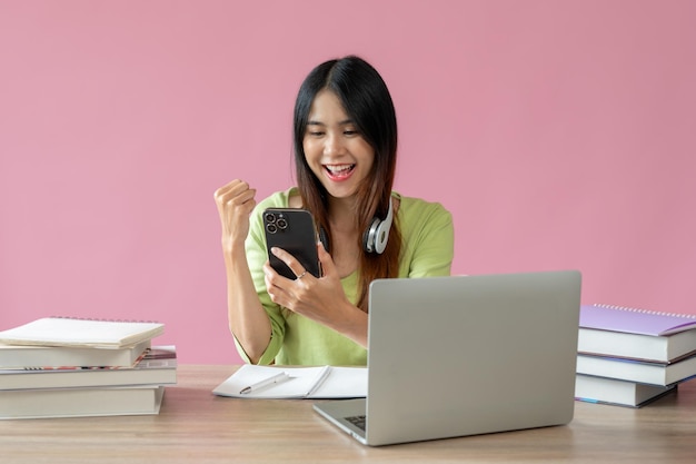 Une fille asiatique positive montre son poing et regarde l'écran de son smartphone avec un visage heureux