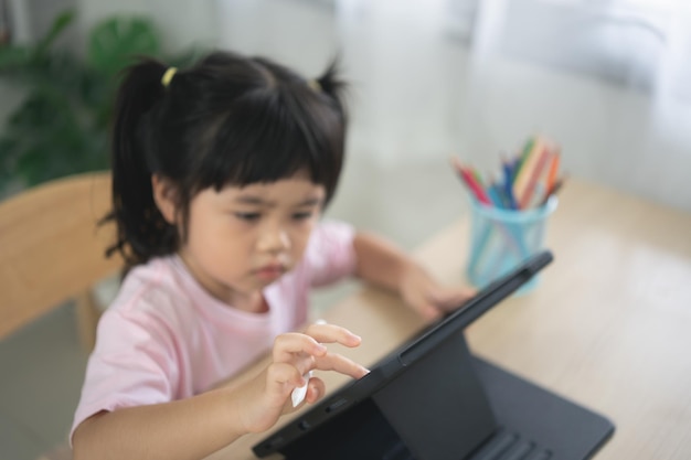 Fille asiatique regardant et touchant sur un écran blanc à l'écran de la tablette concept d'enfants surstimulés avec attention Trop de temps d'écran Jolie fille regardant des vidéos pendant que la télévision fonctionne