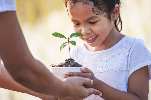 Photo fille asiatique et sa mère tenant de jeunes semis dans le pot de fleurs pour préparer la plantation au sol