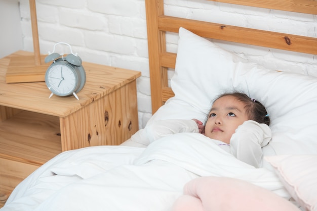 Fille asiatique se réveiller dans son lit avec poupée malheureuse.